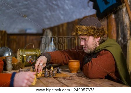 Portrait Of Man In Russian Ethnic Suit Playing Board Game Like Chess. Folk, Competition And Traditio