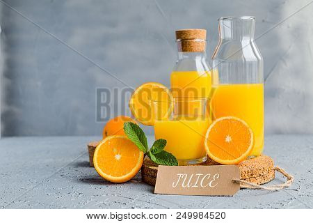 Orange Freshly-squeezed Juice In A Glass And Bottles On Grey Table.