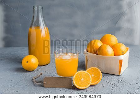 Orange Freshly-squeezed Juice In A Glass And Bottles On Grey Table.