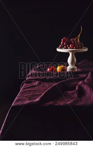 Stand With Grapes And Apples On Table With Drapery On Black