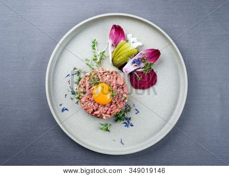 Gourmet tartar raw from beef fillet with yellow of the egg und vegetable as top view on modern design dish