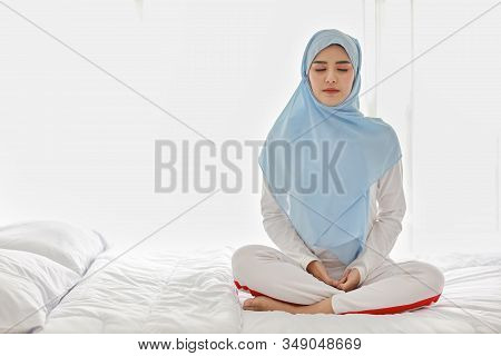 Close Up Young Asian Muslim Woman Sitting On Bed And Enjoying Meditation. Beautiful Girl In Sleepwea