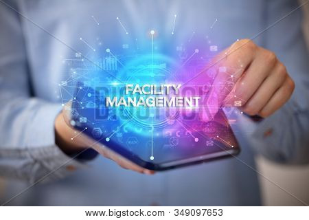Businessman holding a foldable smartphone with FACILITY MANAGEMENT inscription, new business concept