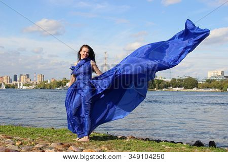 A Woman In A Long Blue Classic Dress That Fluttered In The Wind, Selective Focus. River