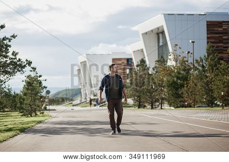 Handsome Brutal Man Walks Next To Modern University Buildings