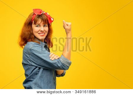 Smiling Middle Aged Woman With A Clenched Fist Rolling Up Her Sleeve On Yellow Background, Copy Spac