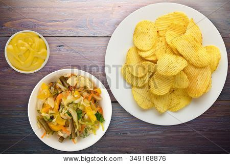 Potato Chips On A White Plate With Vegetarion Salad. Chips On A Purple Wooden Background Top View.