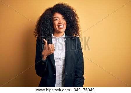 Young beautiful african american business woman with afro hair wearing elegant jacket doing happy thumbs up gesture with hand. Approving expression looking at the camera showing success.