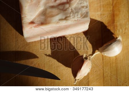 The Whole Large Piece Of Lard, A Knife And Two Cloves Of Garlic Lies On The Table.