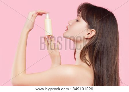 Beauty Woman Face. Close Up Of Young Asian Woman With Fresh Skin Holding A Bottle Of Cream In Hand. 