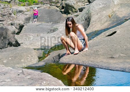 Attractive Teenage Girl Sitting On Rock By Rock Pool Looking At Reflection In Water  At Mclaren Fall