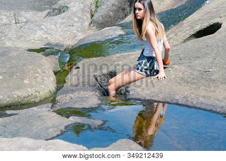 Attractive Teenage Girl Sitting On Rock With Legs Over Edge In Water At Mclaren Falls Tauranga New Z