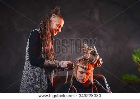 Woman With Long Dreadlocks Is Making Dreads For Blond Girl At Dark Room.