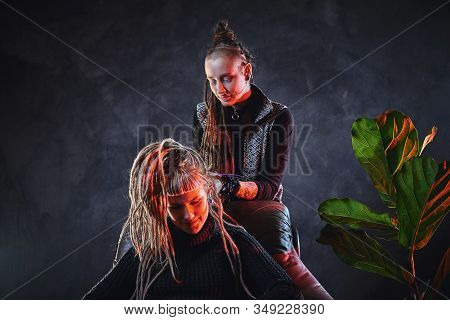 Woman With Long Dreadlocks Is Making Dreads For Blond Girl At Dark Room.