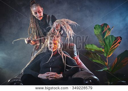 In A Misty Room Full Of Smoke Dread Master Is Making A Dreadlocks For Blond Girl.