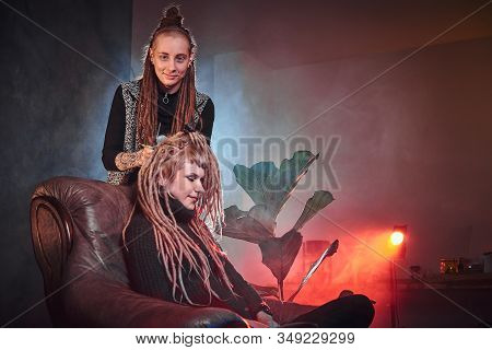 Attractive Dreadlock Master Is Working On Dreads For Pretty Blond Girl In The Dark Room.
