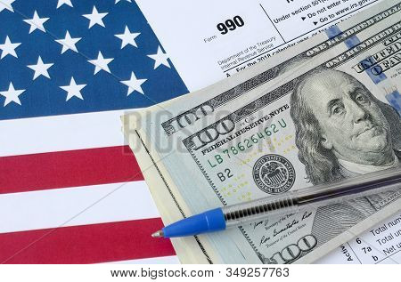 Form 990 Return Of Organization Exempt From Income Tax And Blue Pen With Dollar Bills Lies On United
