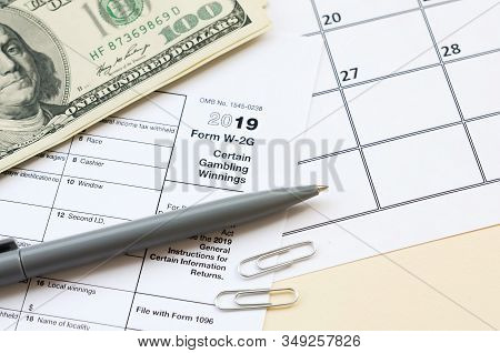 Irs Form W-2g Certain Gambling Winning Blank Lies With Pen And Many Hundred Dollar Bills On Calendar