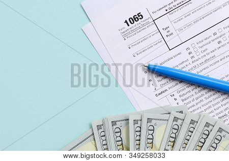 1065 Tax Form Lies Near Hundred Dollar Bills And Blue Pen On A Light Blue Background. Us Return For 