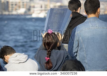 Little Girl Looking At Landscape With Binoculars. Withdrew From Behind. There Are People Around. Eve
