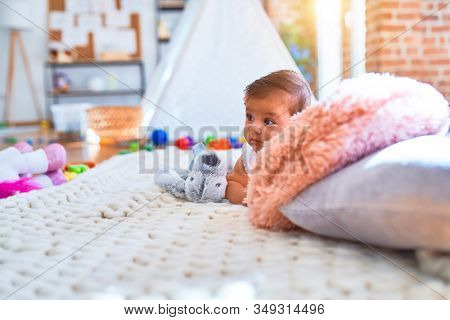 Beautiful infant happy at kindergarten around colorful toys lying on blacket