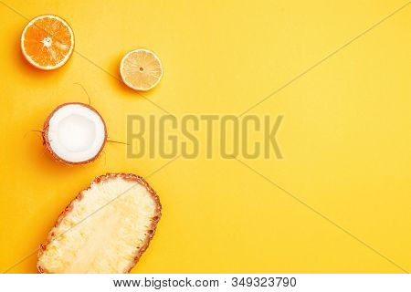 Top View Of Assorted Exotic Fruits On A Yellow Background. Pineapple, Coconut, Orange And Lemon Half
