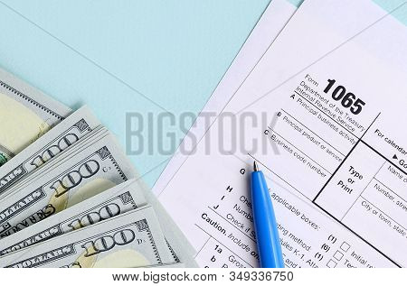 1065 Tax Form Lies Near Hundred Dollar Bills And Blue Pen On A Light Blue Background. Us Return For 
