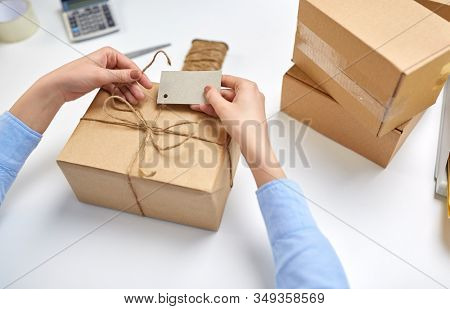 delivery, mail service, people and shipment concept - close up of female hands tying name tag to parcel box at post office
