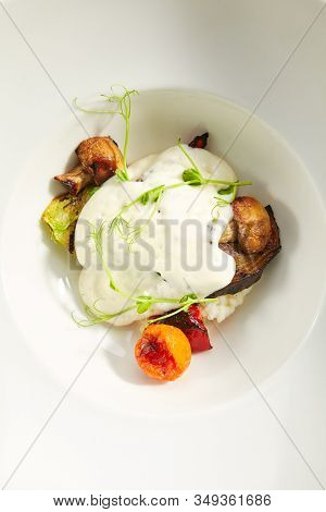Risotto with grilled vegetables, carnaroli rice and cheese foam on white restaurant plate isolated. Traditional Italy rissoto or vegetable paella with cooked eggplants, mushrooms and greens topview