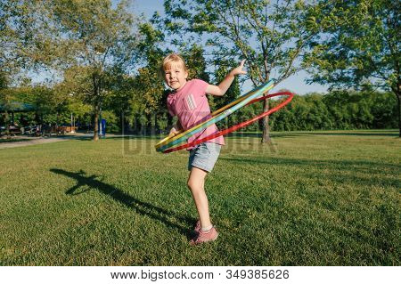 Cute Smiling Caucasian Preschool Girl Playing With Hoola Hoop In Park Outside. Kids Sport Activity. 