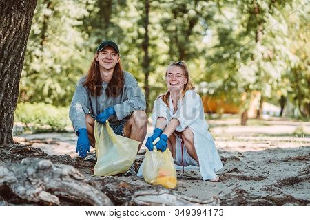 Man And Woman Picking Up Trash From The Park. They Collecting The Litter In Garbage Bag