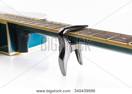 A Capo On Strings Of A Fretboard Of Classic Acoustic Guitar, On A White Background, Close-up.