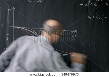 Math teacher drawing fuction graph on a blackboard during mathclass (motion blurred image)