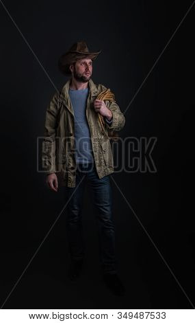 Cowboy In A Wide-brimmed Hat And Jacket With A Lasso On His Shoulder Posing On A Dark Background