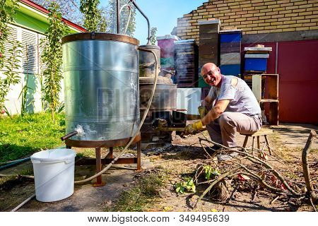 Man Throws Dry Branches Into The Firebox Of A Homemade Distillery Making Moonshine Schnapps, Alcohol