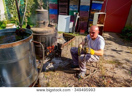 Man Throws Dry Branches Into The Firebox Of A Homemade Distillery Making Moonshine Schnapps, Alcohol