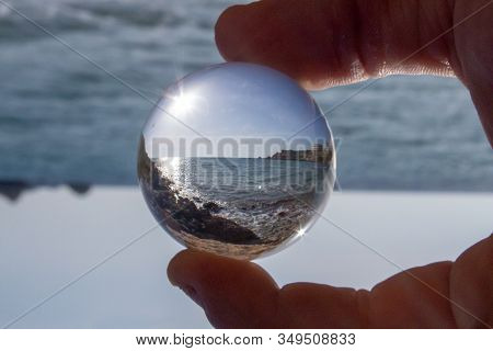 A Crystal Ball Held Between Two Fingers, Reflecting A Beach On A Sunny Day