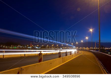 Light Trails A Long A Highway In The Netherlands. The Empty Sidewalk Is Lit By Street Lights