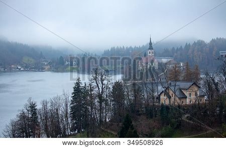 The Bled Chapel And Some Village Houses In The Mist Behind The Trees On A Cold Morning