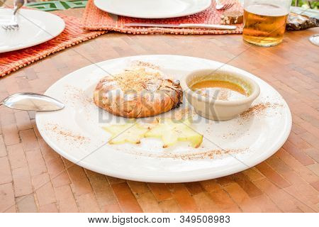 Moroccan Chicken Bisteeya On A White Dish Decorated With Fuit And Sauce