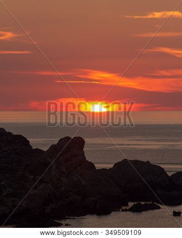 Setting Sun And Silhouette Rocks Foreground. Negative Space