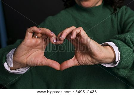 Woman Shows A Heart With Her Hands. Shooting In The Studio On A Black Background. The Instigation Of
