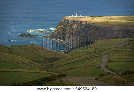 Beautiful View Of Green Fields And Single White Lighthouse Standing On Steep Brink Of Sea Coast. Bac