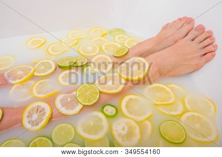 Girl Takes A Milk Bath With Lemons And Limes. Citrus Spa. Body Care. Skin Whitening. Womens Feet.