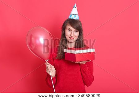 Indoor Picture Of Magnetic Lovely Young Woman Having Holiday Cap On Head, Holding Red Baloon And Red
