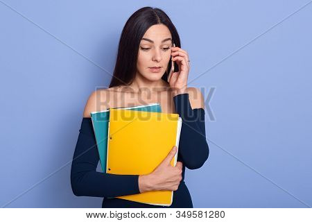 Photo Of Caucasian Businesswoman With Two Paper Folders In Hands, Talking Via Mobile Phone With Asto