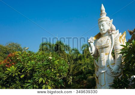White sculpture of Spirit (Nat) guard surrounded by tropical trees at Kyauktawgyi Pagoda complex in Mandalay, Myanmar