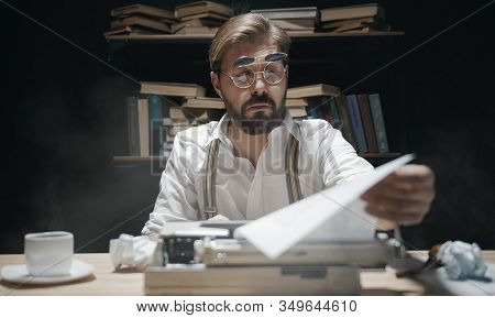 Author In Double Flip-up Eyeglasses Looking At Typescript Checking His Work Sitting In Dark Room