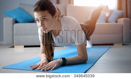 Exercising Girl Do Forearm One-legged Plank On Yoga Mat In Living Room, Front View, Selective Focus