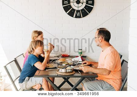 Family Having Lunch On The Balcony, Father And Kids Eating Homemade Humburgers